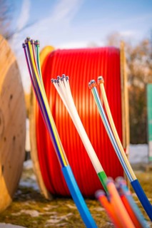 Colourful cables in front of large, red cable spools in a winter environment, fibre-optic