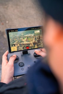 Person controls a drone with a remote control whose screen shows a city, fiberglass groundbreaking,