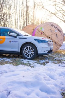 A car stands next to large rolls of cable on a snow-covered meadow in winter, fibreglass