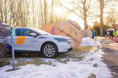 A car is parked next to large cable drums in a wintry environment with construction work,
