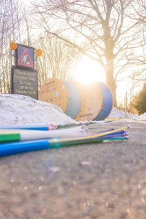Colored cables in front of cable rolls in sunlight along a snowy road, fiberglass groundbreaking,