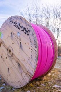 A large pink cable reel stands in a meadow under a blue sky in winter, fiberglass groundbreaking,