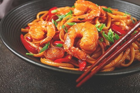 Udon stir-fry shrimp noodles with red bell pepper and green onion, served in a black bowl, with