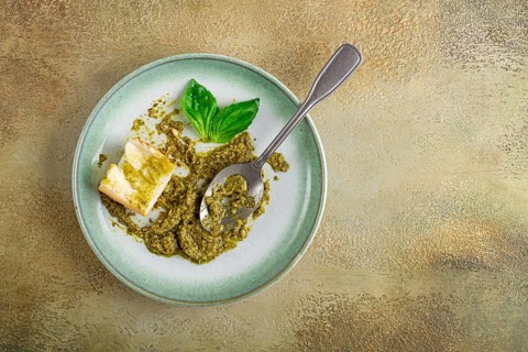 On a platter is a pesto sauce made from fresh basil, with a slice of bread and a spoon on a plate.