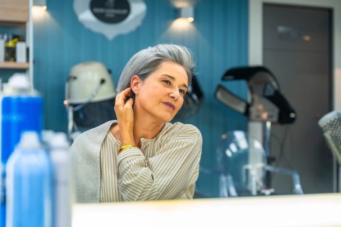 Senior woman with silver hair smiles, admiring her stylish short haircut in a salon mirror, feeling