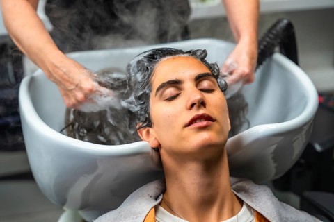 Young woman relaxing with closed eyes while hairdresser hands gently wash her hair with shampoo and