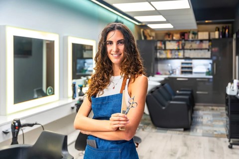 Professional female hairdresser in a modern salon smiling confidently while holding scissors and a