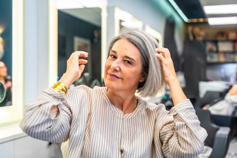 Senior woman smiling and touching her healthy gray hair, sitting in a modern hair salon, ready for