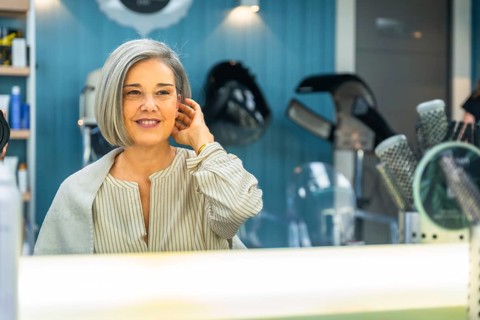 Senior woman looking at her reflection in the salon mirror, smiling and admiring her new short
