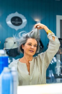 Mature woman looking at her reflection and touching her natural gray hair after a recent blow dry