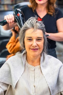 Mature woman sitting in a hair salon during a blow dry session, smiling confidently while a