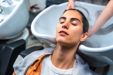 Woman closing her eyes while relaxing and receiving a professional hair wash and steam treatment at