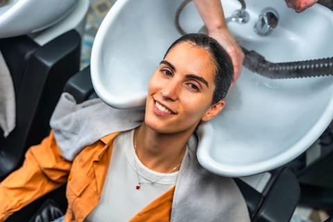 Young woman smiling and relaxing as a hairdresser shampoos and rinses her hair at a professional