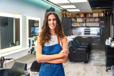 Woman hairstylist entrepreneur smiling, standing in a small business hair salon, holding hair