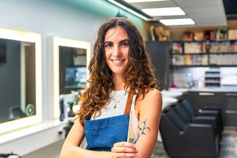 Professional woman with curly hair wearing an apron and holding hairdressing scissors and a comb,