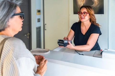 Salon receptionist smiling and processing a contactless credit card payment at the front desk for a