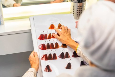Client selecting desired hair dye shade from a detailed color chart while sitting in a hair salon,
