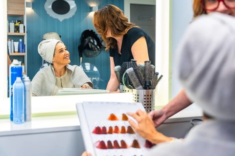 Woman client in a salon chair with a towel wrapped around her hair, looking at her reflection and