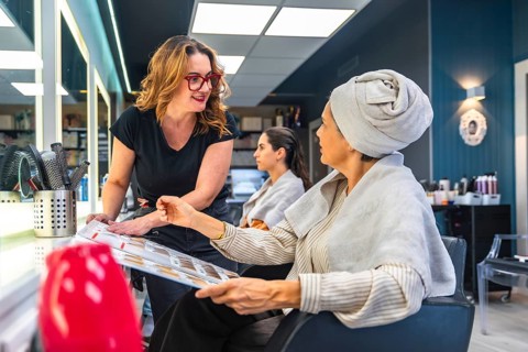 Hairdresser and female client discussing hair color and style options using a color chart,