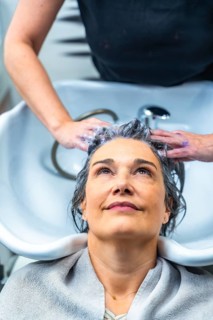 Woman with gray hair receiving a shampoo and head massage from a hairstylist at a modern hair