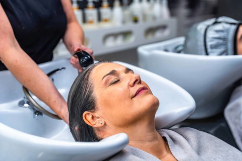 Woman with closed eyes relaxing during a hair wash service at a beauty salon, symbolizing self