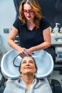 Hair stylist washing a mature woman's hair at the shampoo sink, creating a moment of self care,