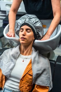 Relaxing woman with eyes closed wearing a heat cap during a professional hair treatment at a modern