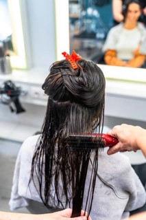 Professional hairdresser gently brushing wet hair of a female client during conditioning and