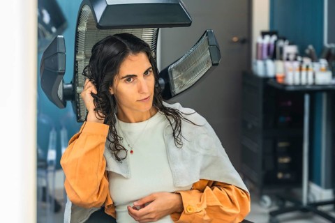 Young woman seated under a professional salon hair dryer, receiving a pampering hair treatment