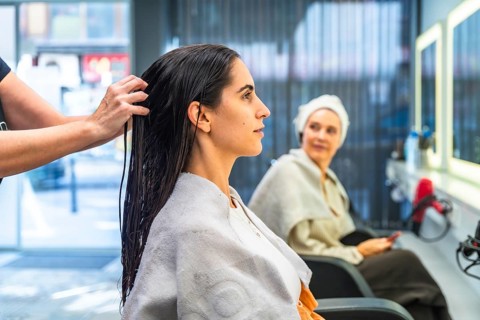 Hairdresser applying hair treatment to a young woman's wet, dark hair, highlighting beauty, care,