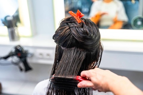 Hairdresser's hand brushing through long, wet hair of a woman, carefully sectioning strands with