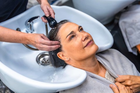 Senior woman smiling as a professional hairdresser washes and massages her hair at a salon sink,