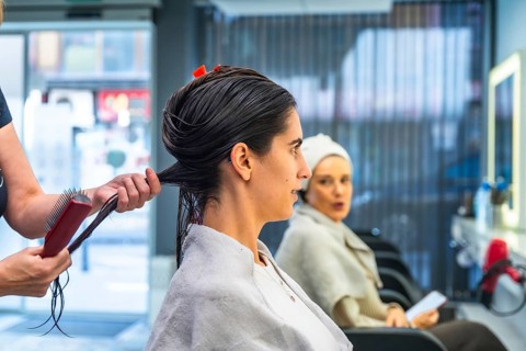 Hairdresser's hands dividing and combing a young woman's wet dark hair, preparing for a haircut or