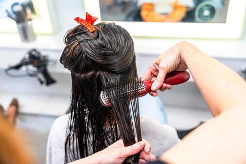 Professional hairdresser brushing through wet, dark long hair with clips, preparing sections for