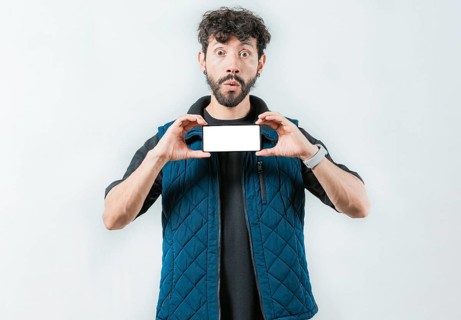 A surprised bearded man showing phone screen isolated. Shocked bearded guy showing promotion on