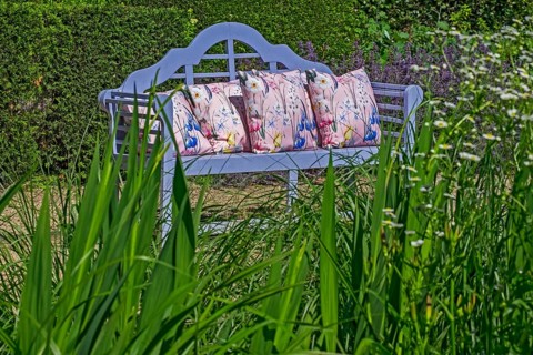 Blue garden bench with decorative cushions surrounded by plants and shrubs, Netherlands