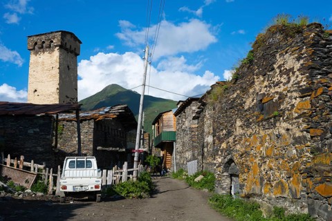 A village street with a white wagon, surrounded by stone buildings and power poles, defensive