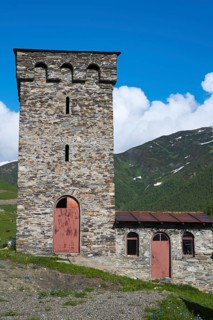 Old stone tower and small building against a mountain backdrop under a deep blue sky, defensive