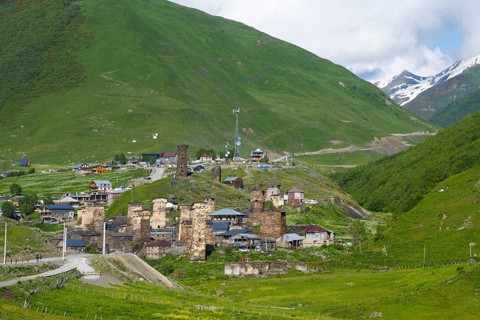 Mountain village with old stone towers surrounded by green hills and mountains under a partly