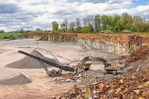 Open pit mining with an excavator at a stone crusher and a conveyor for loading stones