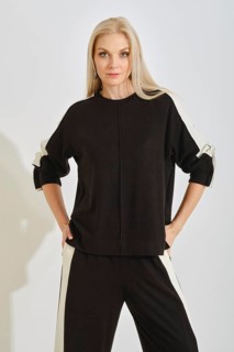 A woman stands with a confident pose wearing a comfortable black tracksuit with white stripes on
