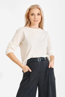 A woman poses with hands in pockets wearing a light shirt and dark pants. She has long blonde hair