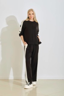 A woman stands confidently in a stylish black tracksuit featuring white stripes along the sides.