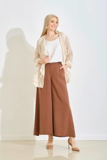 A smiling woman stands gracefully in a bright, minimalist studio, dressed in a light top and