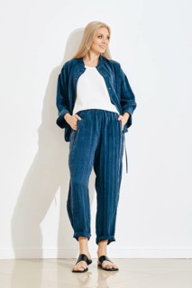 A woman is standing against a white wall in a bright room. She wears a blue pants and jacket with a