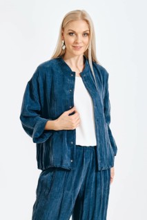 A woman stands in a studio wearing a blue outfit. She poses confidently with a smile. The