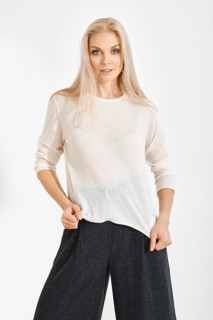 A model stands in a studio wearing a white top and dark wide-leg pants. She showcases the clothing