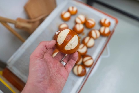 Hand holding a baked pretzel over a tray with other pretzels, bake rolls, Haselstaller Hof,