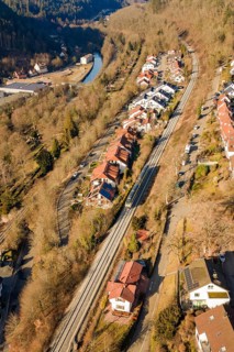 Aerial view of a village with railroad tracks, surrounded by forests and a river, test run on the