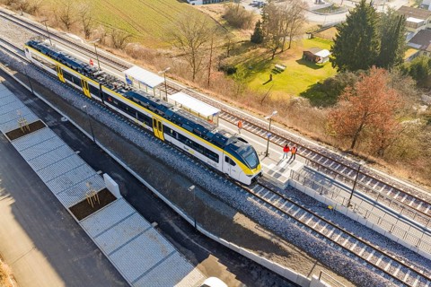 Train at train station surrounded by people, landscape with fields and trees, test run on the new